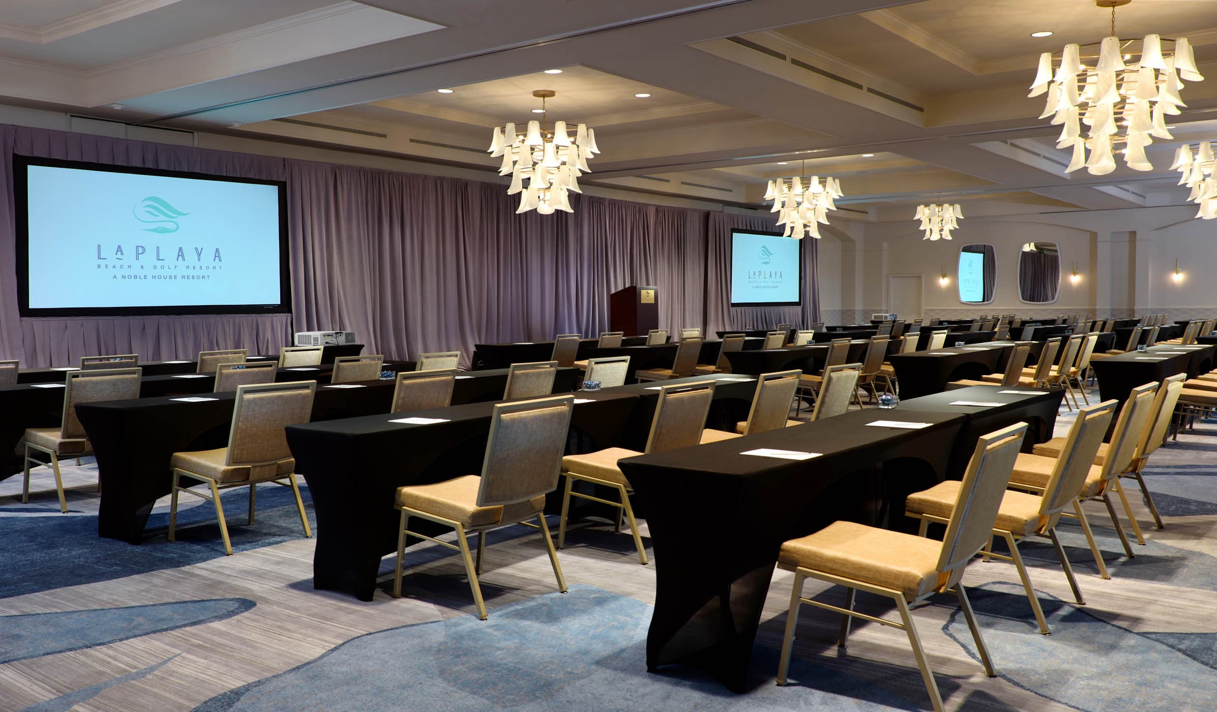 A large room set up with tables and 2 screens for a meeting at LaPlay