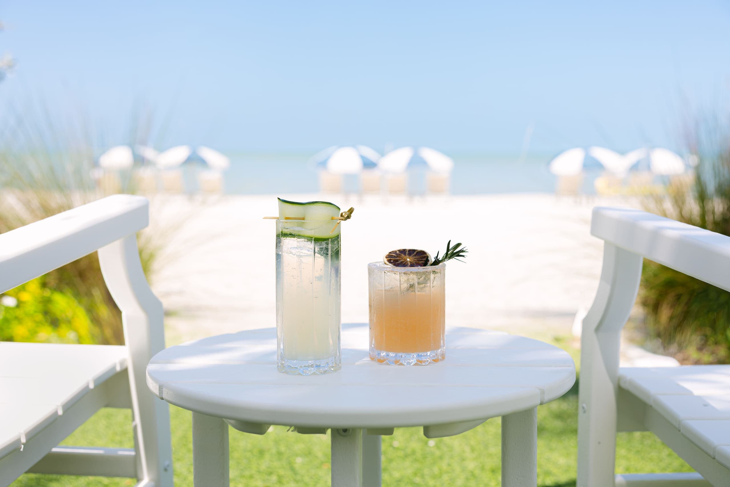 2 cocktails on a small table beside 2 lounge chairs on the lawn