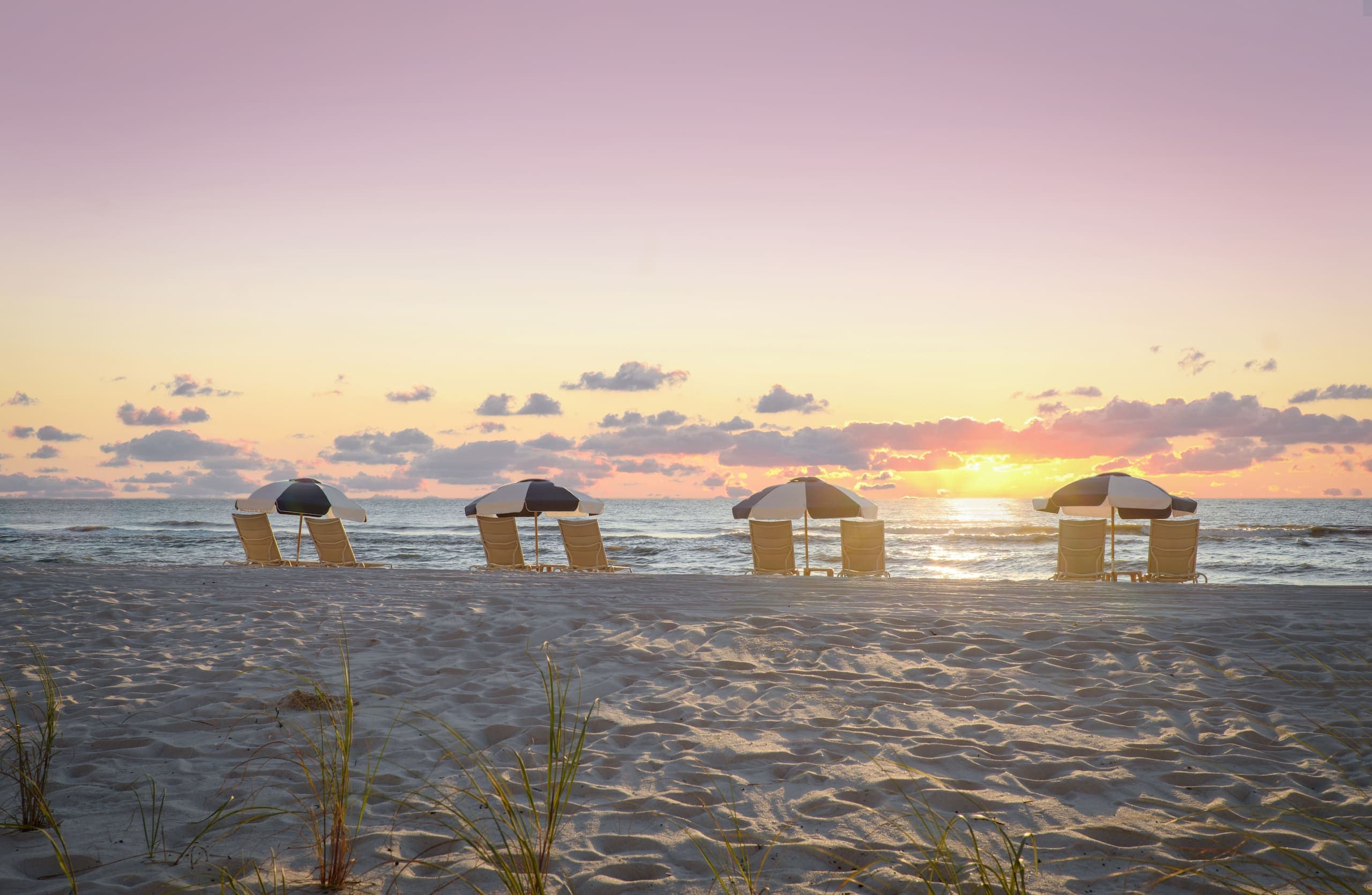 4 beach umbrellas and chairs on the beach at sunset