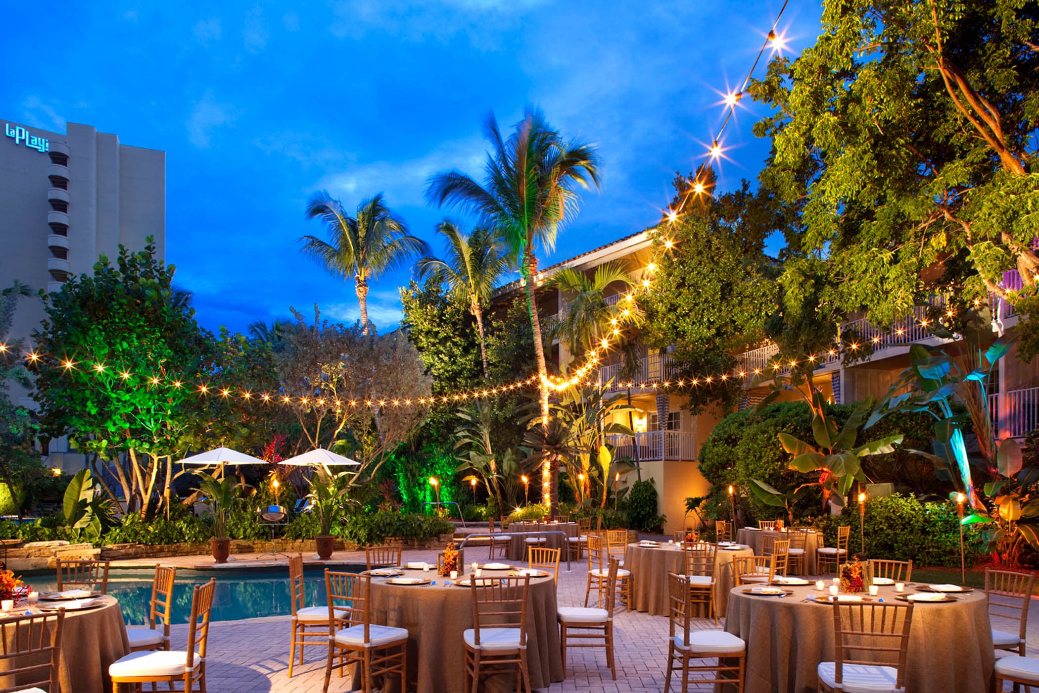 A pool with table set up around it for a function at night with gorgeous string lights