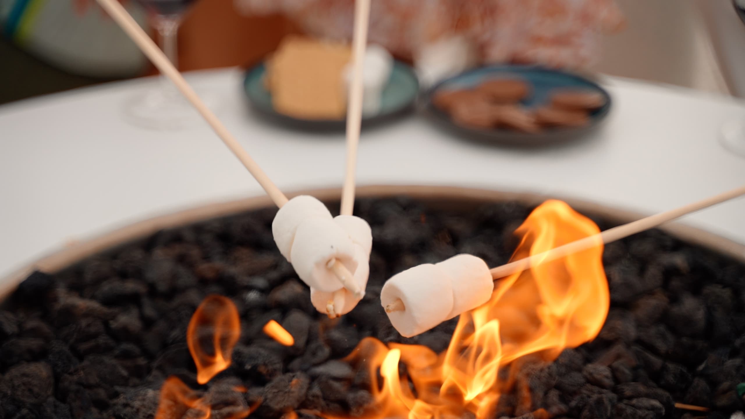 3 sticks with marshmallows on them being roasted in the fire pit