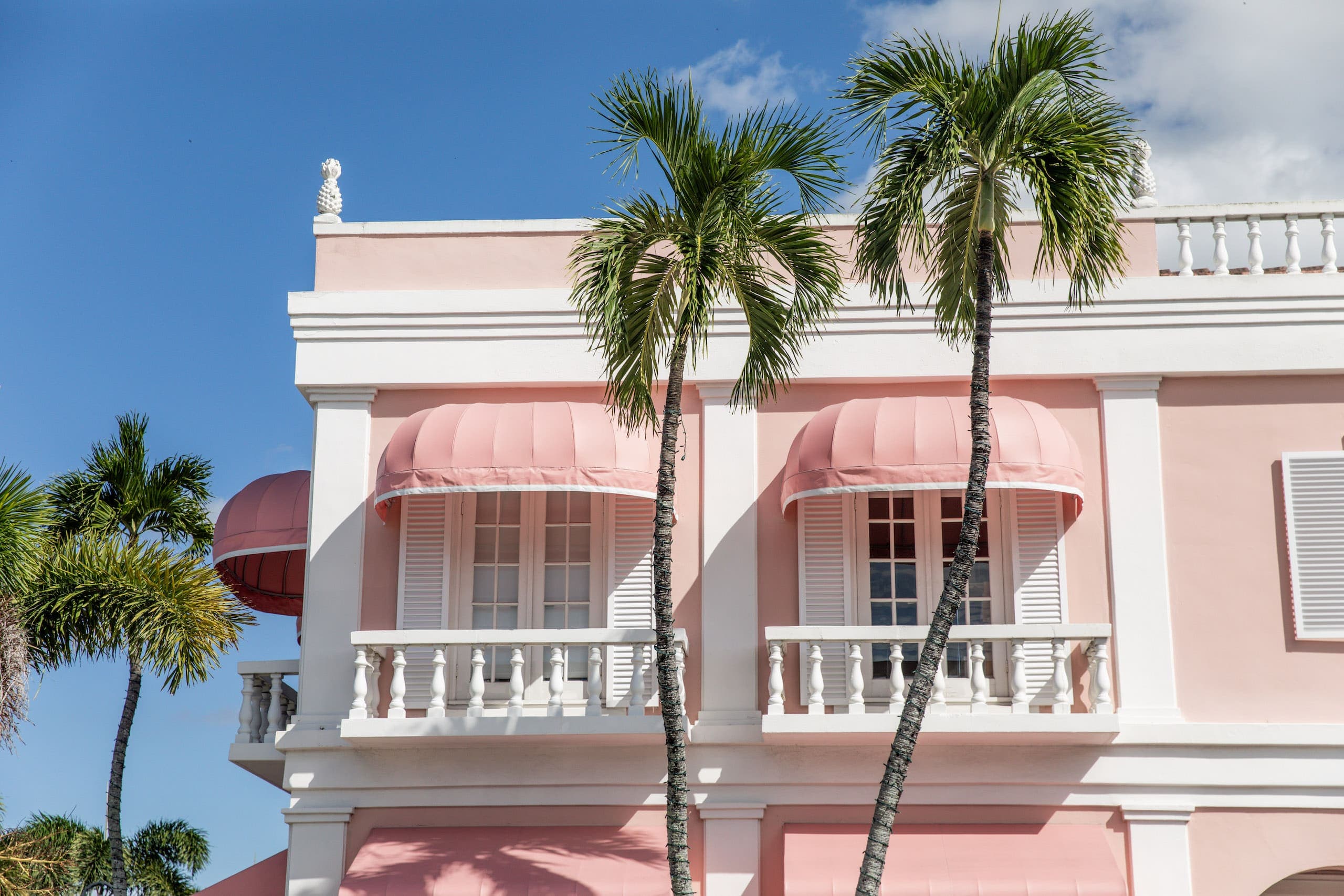 The side of a pink and white building with a palm tree out front