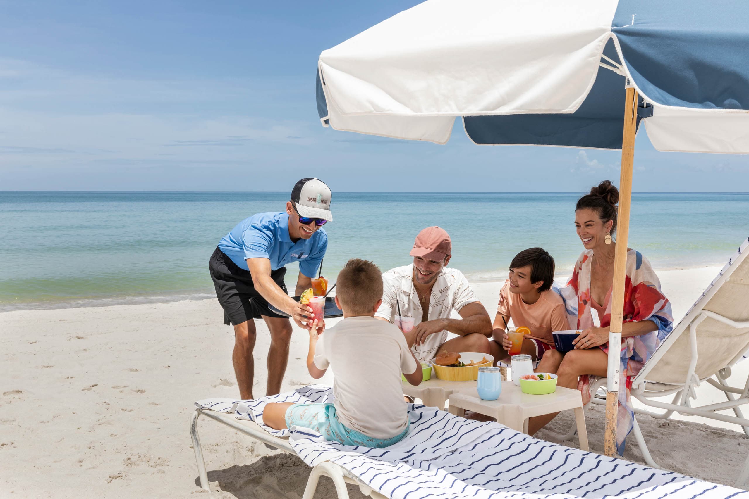 A beach attendant serving drinks and food to a family at the beach