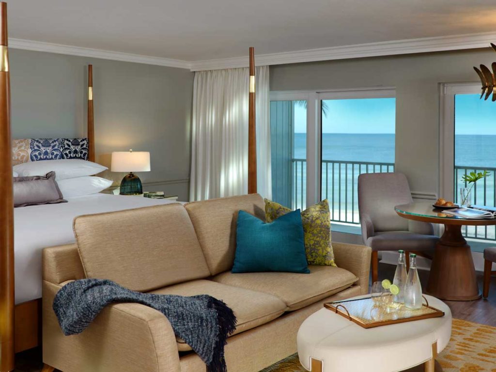 King sized bed, couch, eating area, and balcony with ocean views in Naples, FL