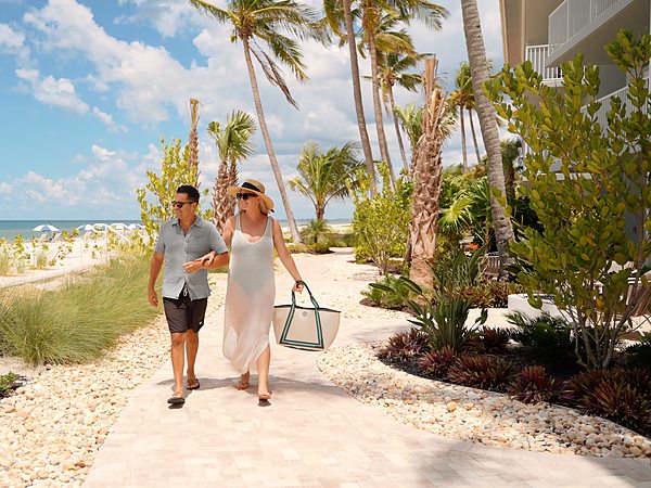 Couple walking the beachfront path beside the guest building at LaPlaya Beach & Golf Resort in Naples, FL, with palm trees and Gulf views
